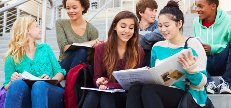 Group of high school students sitting outside building of one of the best schools their parents could find when moving.