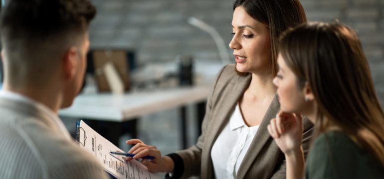 Female real estate agent talking to a couple while making plans about their future home purchase during a meeting in the office.