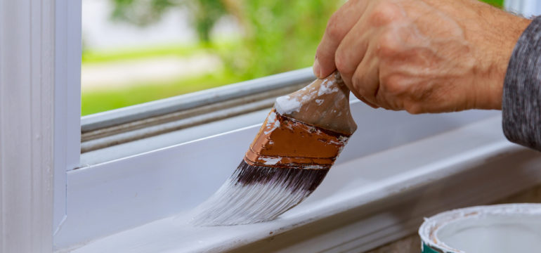 Painting wooden windows with paintbrush while windows may get stuck when the trim dries.