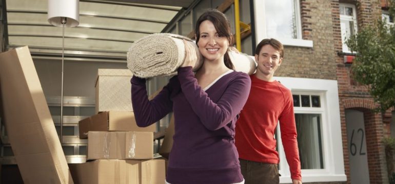 Portrait of happy young couple carrying rolled carpet from a rental truck that's insured.