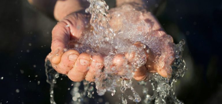 Hands washing with well water pouring from a spigot.