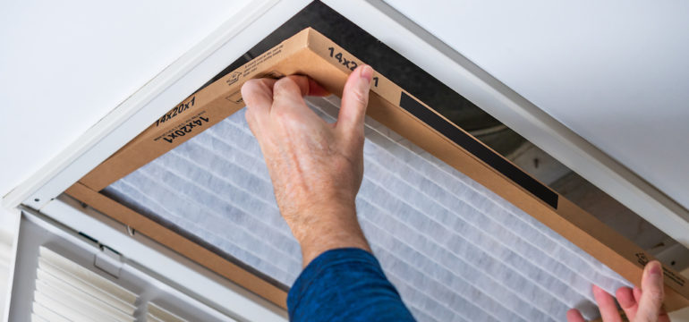 A man replacing a dirty HVAC air filter in a ceiling vent. Home air duct cleaning for clean air.