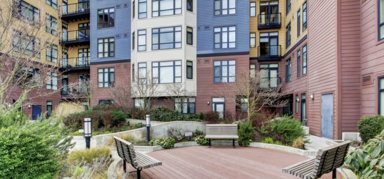Empty benches near a ground-floor apartment in a urban, multi-unit building with several floors.