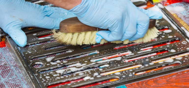 Grill cleaning with blue gloved hands scrubbing grates with a brush.