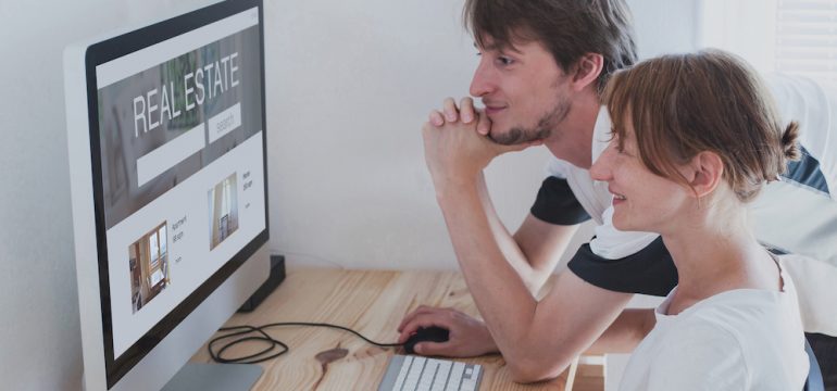 A couple conducting a online home search on a real estate portal on their home desktop computer.