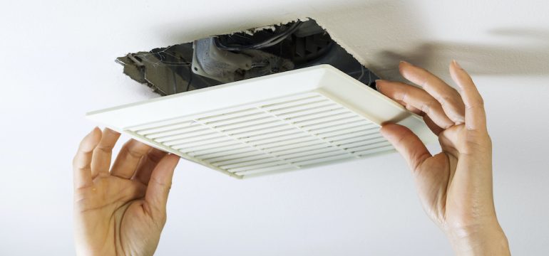 Close up horizontal photo of female hands removing bathroom exhaust fan cover from ceiling to clean it.