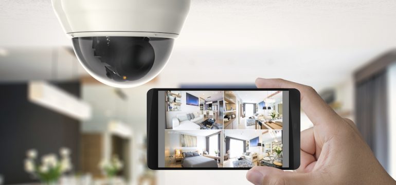 A hand holding a cellular phone connected to a home security camera.