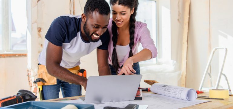Young african american woman pointing at laptop screen to boyfriend during renovation of home. Wondering about renovating or buying a new home.