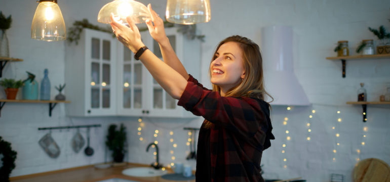 Young happy woman twists a light bulb in the kitchen lamp with the correct light bulb wattage.