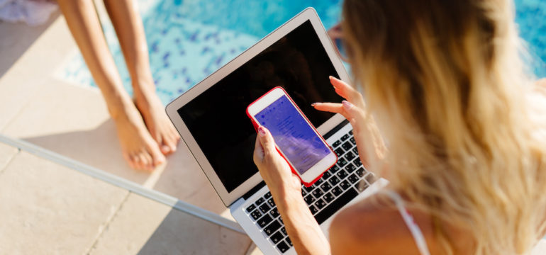 Guest users using laptop and smartphone remotely near swimming pool. multiple devices.