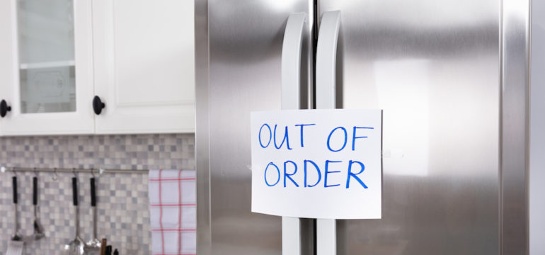 Written text "Out Of Order" message on paper taped on closed refrigerator door In a kitchen. Demonstrates what to do with a broken appliance.