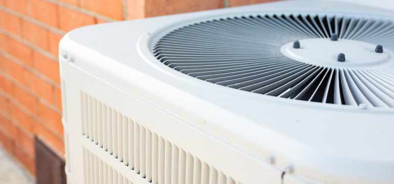 A view of an air conditioner condenser unit in the backyard of a home.