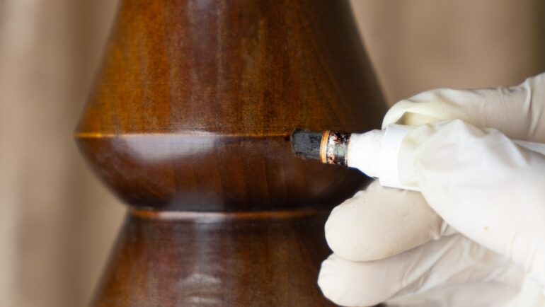 Repairing a flaw in a piece of scratched wooden furniture table leg with a special marker. A close-up photo of restoration of furniture and wooden surfaces.