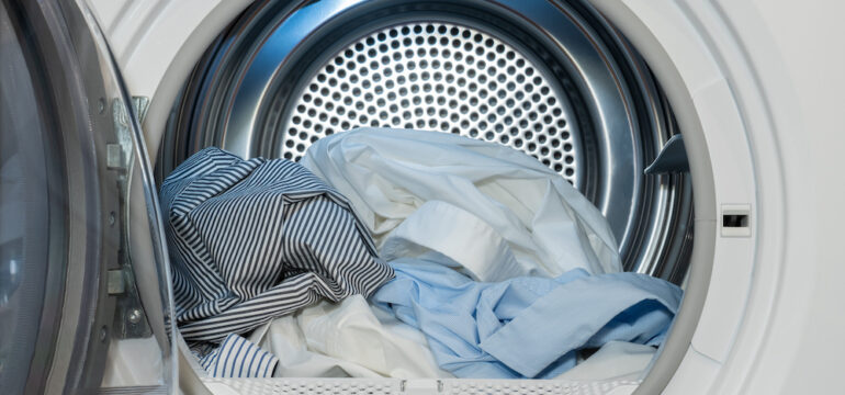Close up view on clothes dryer with washed and dried shirts in and door open.