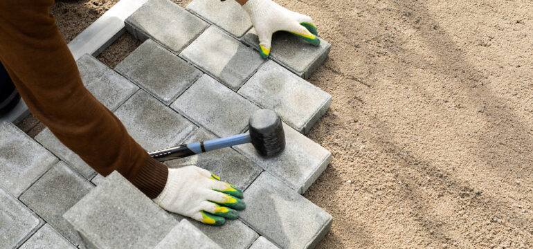 Hands of a worker installing a paver patio with a rubber hammer.