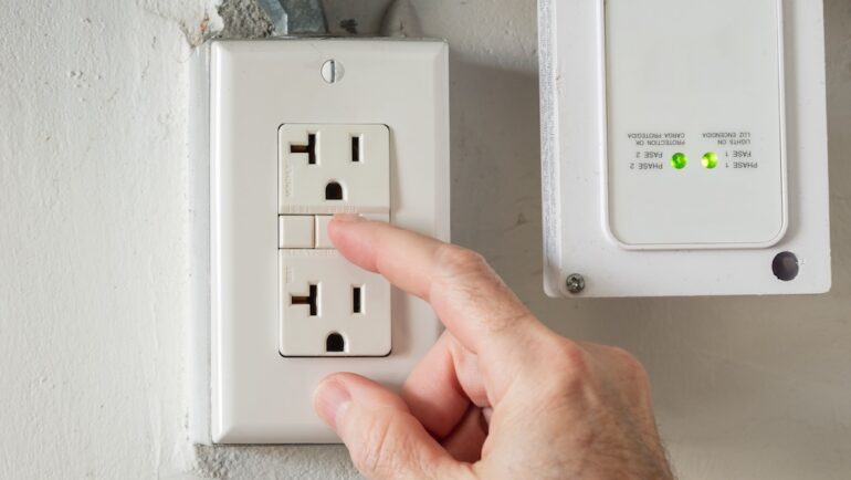 Closeup of hand resetting tripped GFI electricity outlet in home electrical system. DIY maintenance tasks.