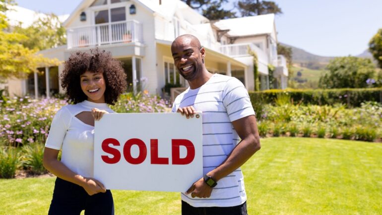 Happy home sellers holding a SOLD sign that use seller concessions to close the purchase of their home.